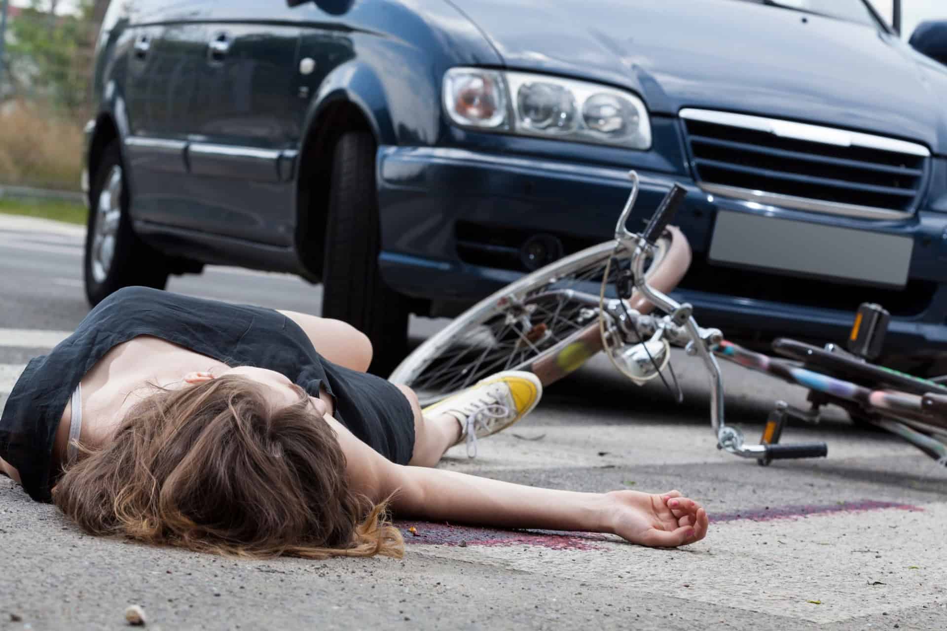 A person lies on the ground next to a fallen bicycle in front of a car at a crosswalk—an unsettling scene that might require the expertise of an attorney.