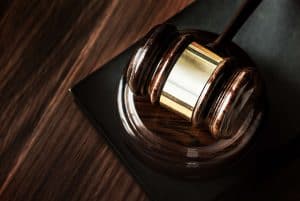 A wooden judge's gavel rests on a matching base, placed on a dark wood surface.