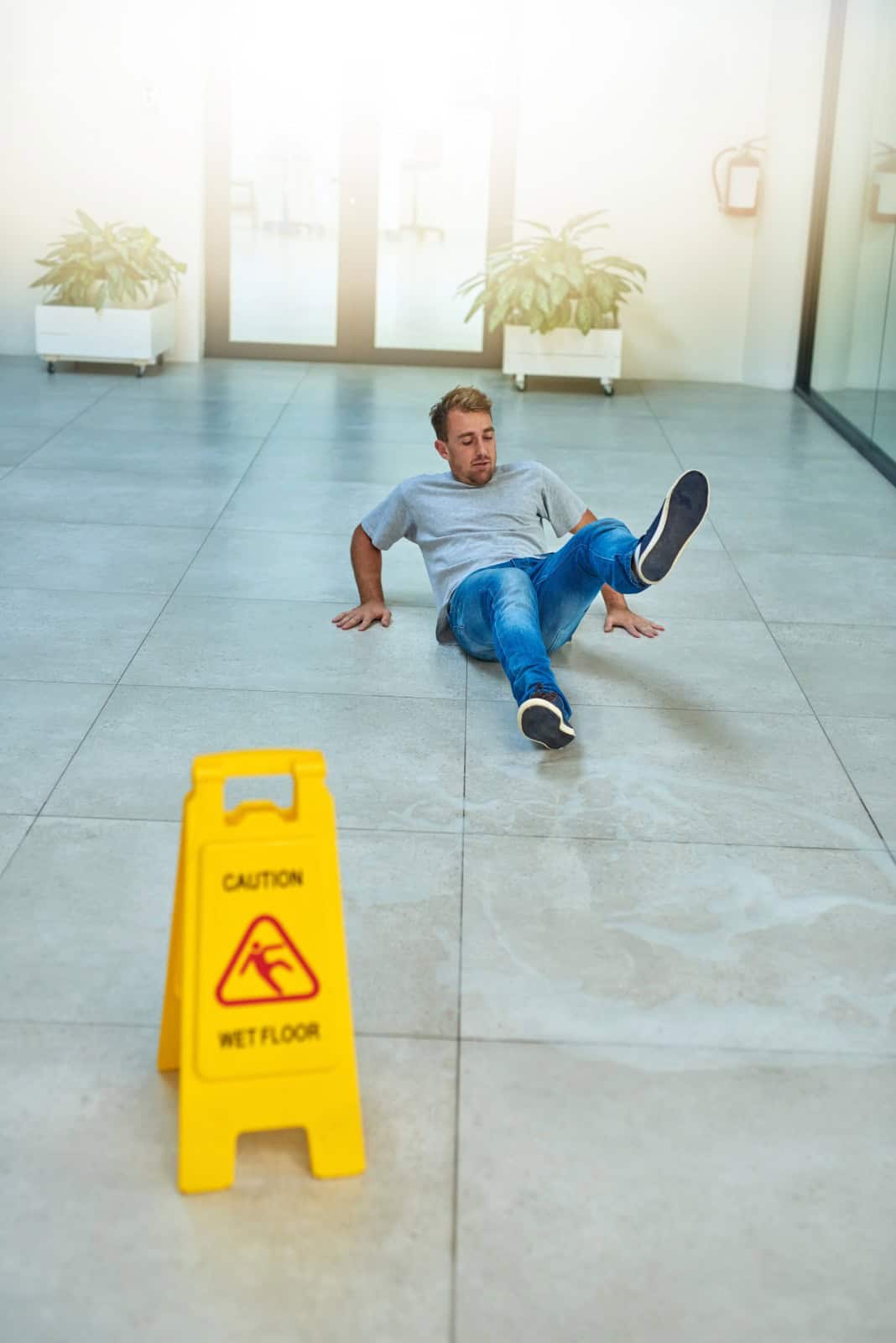 Man slipping on wet floor in a hallway, near a yellow caution sign.