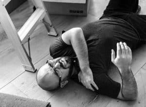 Man lying on the floor near a ladder, holding his shoulder.