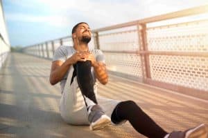 Man sitting on a bridge holding his knee, appearing to be in pain.