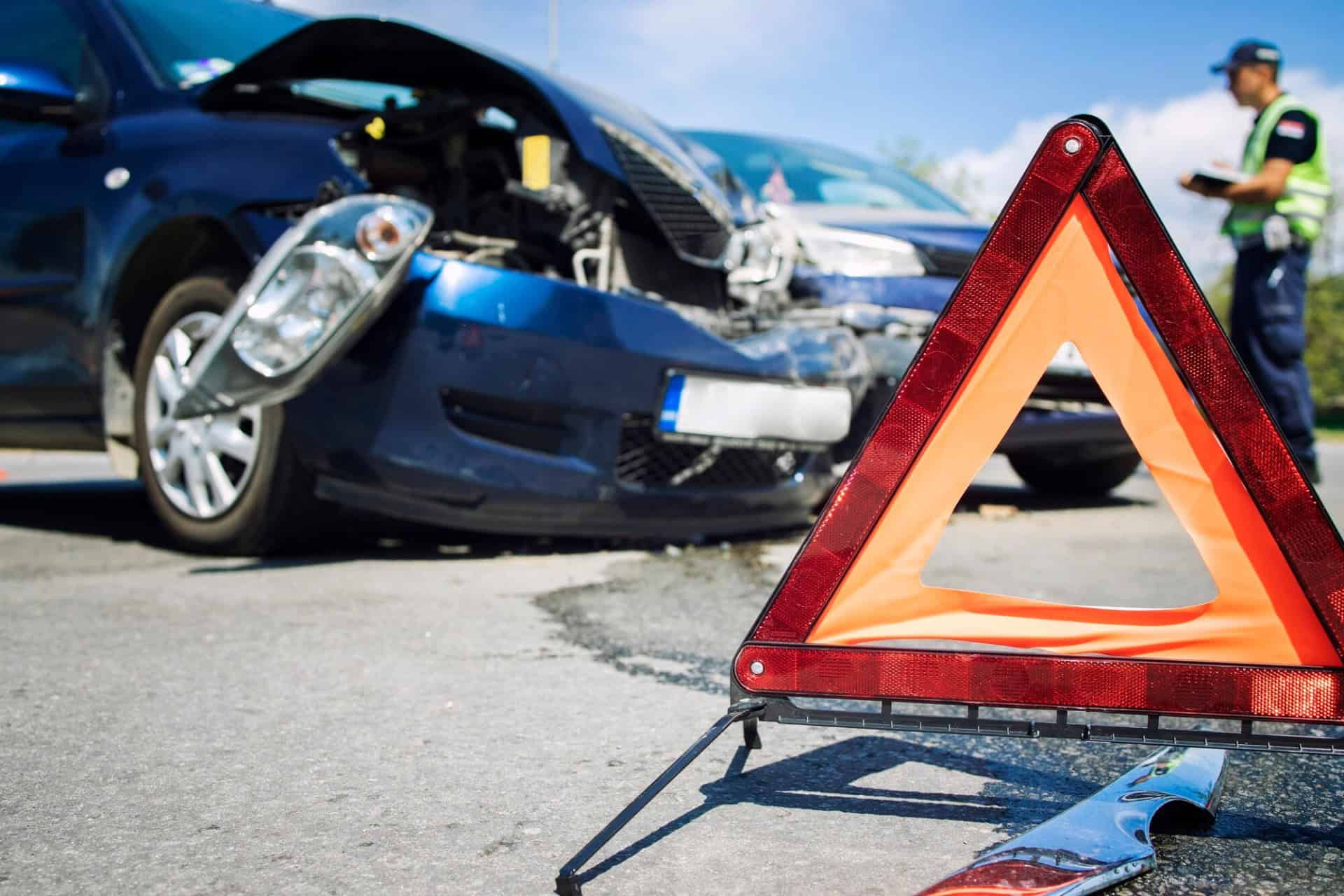 Two cars are involved in an accident on a road. A warning triangle is placed nearby, as a police officer examines the scene. Nearby, an attorney from a local law firm takes notes, ready to assist anyone needing legal counsel.